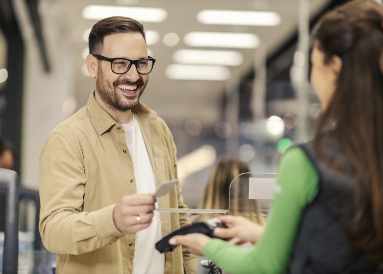 A smiling man is purchasing with credit card on pos terminal at checkout.