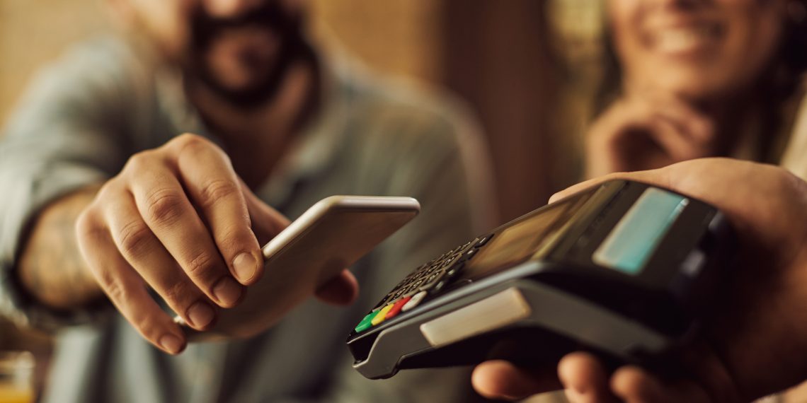 Close-up of man using smart phone while making contactless payment in a cafe.