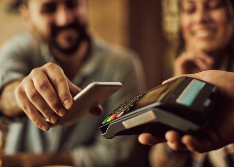 Close-up of man using smart phone while making contactless payment in a cafe.