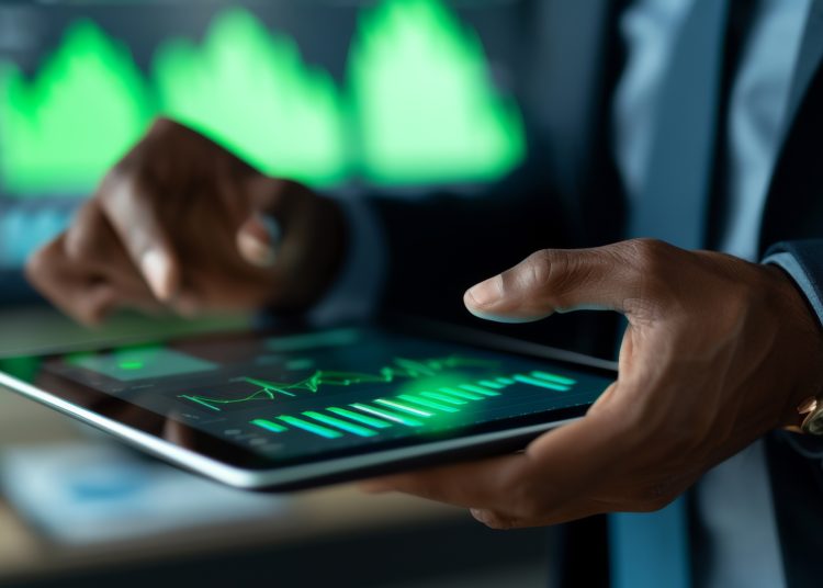 A professional is analyzing financial data on a tablet, interacting with charts and graphs displayed on the screen in a corporate setting.